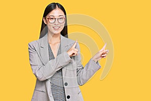 Young chinese woman wearing business clothes smiling and looking at the camera pointing with two hands and fingers to the side