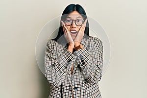 Young chinese woman wearing business style and glasses afraid and shocked, surprise and amazed expression with hands on face