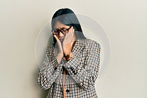 Young chinese woman wearing business style and glasses with sad expression covering face with hands while crying