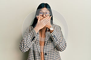 Young chinese woman wearing business style and glasses shocked covering mouth with hands for mistake