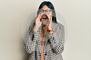Young chinese woman wearing business style and glasses shouting angry out loud with hands over mouth