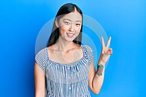 Young chinese woman wearing casual striped t-shirt showing and pointing up with fingers number two while smiling confident and