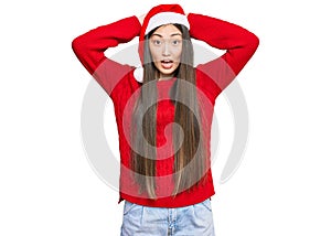 Young chinese woman wearing christmas hat crazy and scared with hands on head, afraid and surprised of shock with open mouth