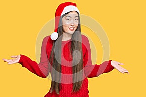 Young chinese woman wearing christmas hat smiling showing both hands open palms, presenting and advertising comparison and balance