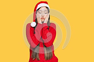 Young chinese woman wearing christmas hat tired hands covering face, depression and sadness, upset and irritated for problem