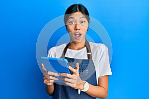 Young chinese woman wearing cook apron using touchpad afraid and shocked with surprise and amazed expression, fear and excited