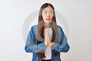 Young chinese woman wearing denim shirt standing over isolated white background begging and praying with hands together with hope