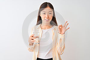 Young chinese woman wearing glasses drinking glass of water over isolated white background doing ok sign with fingers, excellent