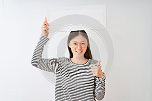 Young chinese woman wearing glasses holding banner over isolated white background happy with big smile doing ok sign, thumb up