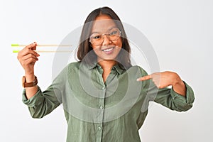 Young chinese woman wearing glasses holding chopsticks over isolated white background with surprise face pointing finger to
