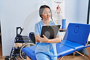 Young chinese woman wearing physiotherapist uniform write on medical report at rehab clinic