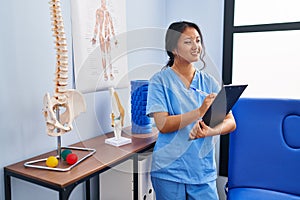 Young chinese woman wearing physiotherapist uniform write on medical report at rehab clinic