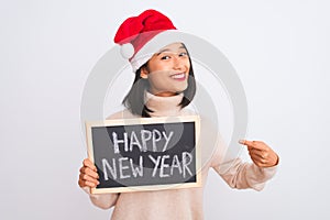 Young chinese woman wearing Santa hat holding blackboard over isolated white background very happy pointing with hand and finger