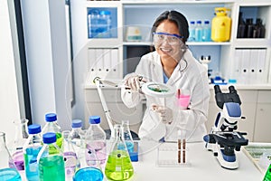 Young chinese woman wearing scientist uniform using loupe at laboratory