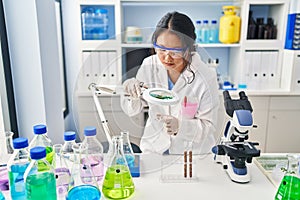 Young chinese woman wearing scientist uniform using loupe at laboratory