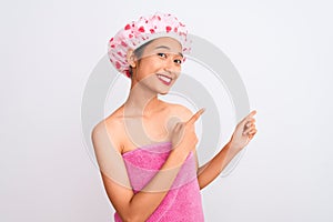 Young chinese woman wearing shower towel and cap bath over isolated white background smiling and looking at the camera pointing