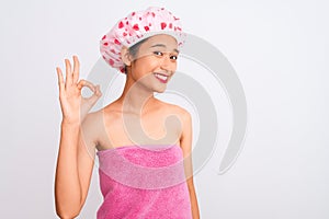 Young chinese woman wearing shower towel and cap bath over isolated white background smiling positive doing ok sign with hand and