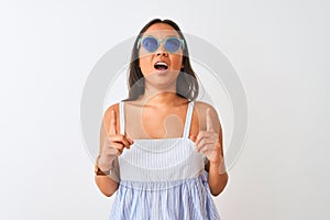 Young chinese woman wearing striped dress and sunglasses over isolated white background amazed and surprised looking up and