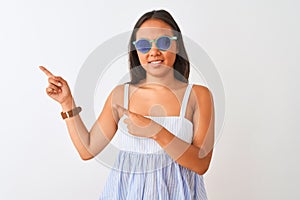 Young chinese woman wearing striped dress and sunglasses over isolated white background smiling and looking at the camera pointing