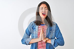 Young chinese woman wearing striped t-shirt and denim shirt over isolated white background begging and praying with hands together