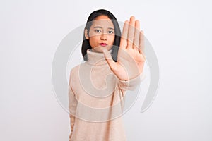 Young chinese woman wearing turtleneck sweater standing over isolated white background doing stop sing with palm of the hand