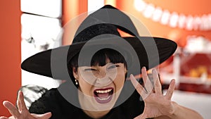 Young chinese woman wearing witch costume doing scare gesture at home