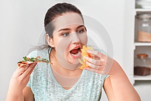 Binge Eating. Chubby girl sitting at kitchen table eating pizza and chips hungry close-up photo