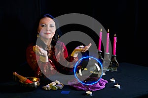 Young clairvoyant and fortune teller with candles in hands in a magic salon on a black background.
