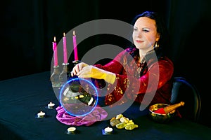 A young clairvoyant and fortuneteller reads the future on a mirror ball in a magic salon on a black background.