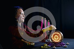 A young clairvoyant and fortuneteller reads the future on a mirror ball in a magic salon on a black background.