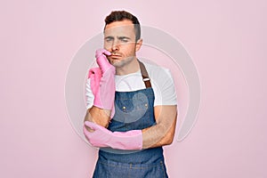 Young cleaner man with blue eyes cleaning wearing apron and gloves over pink background thinking looking tired and bored with