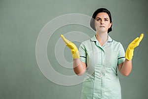 Young cleaning woman with greenapron and black t-shirt and yellow gloves with open arms looking up