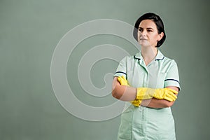 Young cleaning woman wearing a green shirt and yellow glove looking confident hero-shot