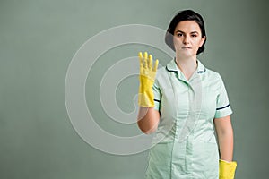 Young cleaning woman wearing a green shirt and yellow gloves counting four with her fingers