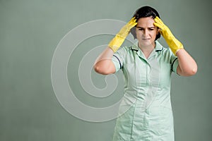 Young cleaning woman wearing a green shirt and yellow gloves has headache