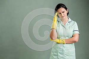 Young cleaning woman wearing a green shirt and yellow gloves has headache