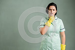 Young cleaning woman wearing a green shirt and yellow gloves has sore throat