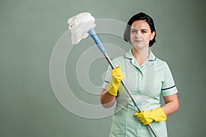 Young cleaning woman wearing a green shirt and yellow gloves holding mop