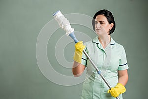 Young cleaning woman wearing a green shirt and yellow gloves holding mop