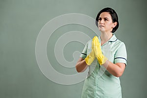 Young cleaning woman wearing a green shirt and yellow gloves praying