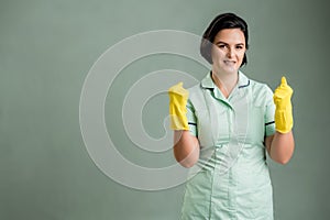 Young cleaning woman wearing a green shirt and yellow gloves raised fists up exclaiming with joy and excitement