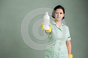 Young cleaning woman wearing a green shirt and yellow gloves showing dishwashing solution