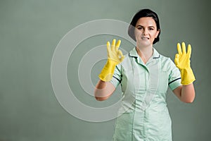 Young cleaning woman wearing a green shirt and yellow gloves showing double OK sign