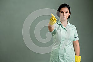 Young cleaning woman wearing a green shirt and yellow gloves showing no with her finger