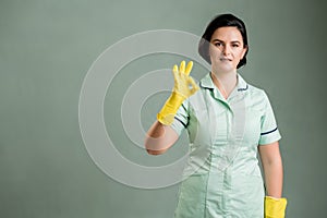 Young cleaning woman wearing a green shirt and yellow gloves showing OK sign