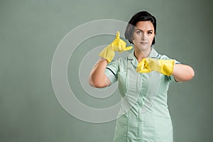 Young cleaning woman wearing a green shirt and yellow gloves showing it`s time gesture
