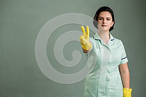 Young cleaning woman wearing a green shirt and yellow gloves showing victory