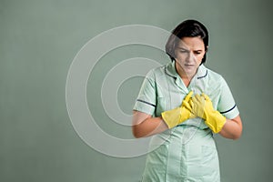 Young cleaning woman wearing a green shirt and yellow gloves suffering heart ache or breast pain, cardiac problems
