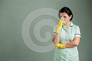 Young cleaning woman wearing a green shirt and yellow gloves wondering