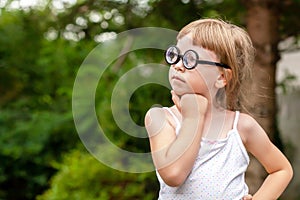 Young clever intelligent school age child, little girl in big quirky glasses thinking, wondering, deep in thought, copy space